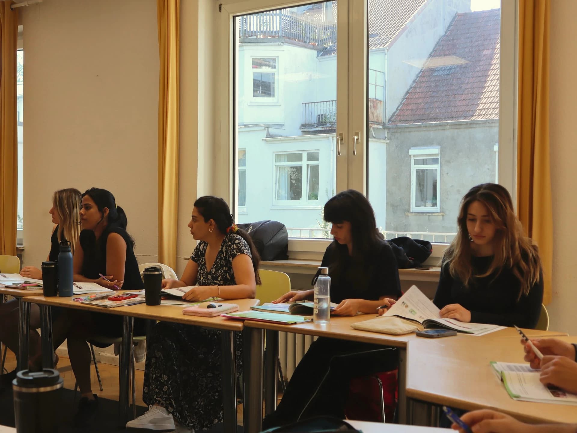 Learners at a long table by the window, following a German lesson