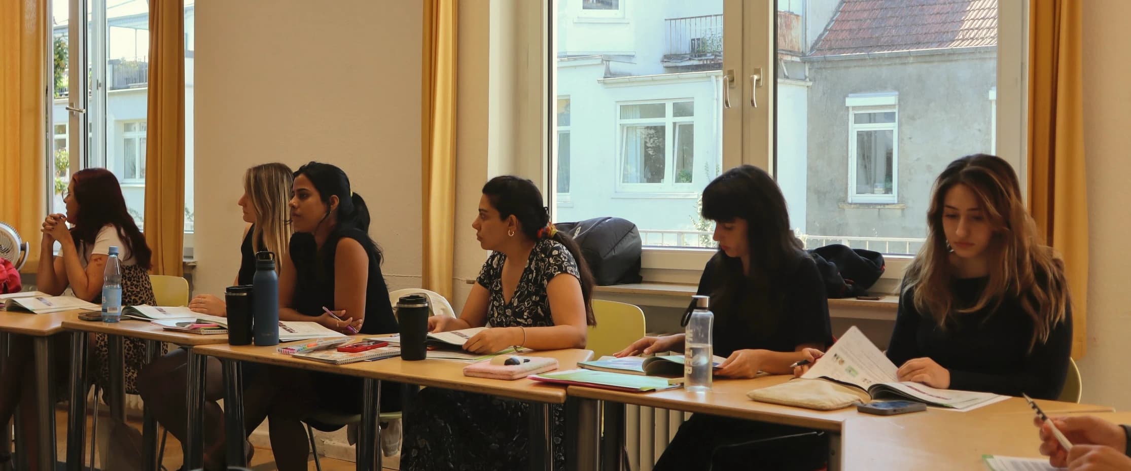 Learners at the long table by the window in a German lesson